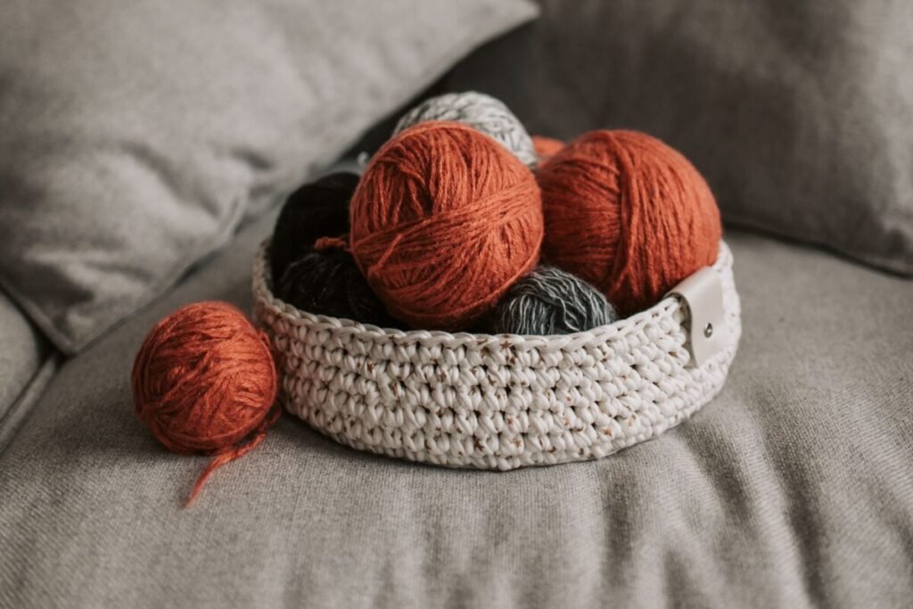 Rust and grey yarn balls in a crocheted basket on a sofa