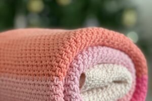 A folded handmade crochet blanket in bright stripes, photographed flat