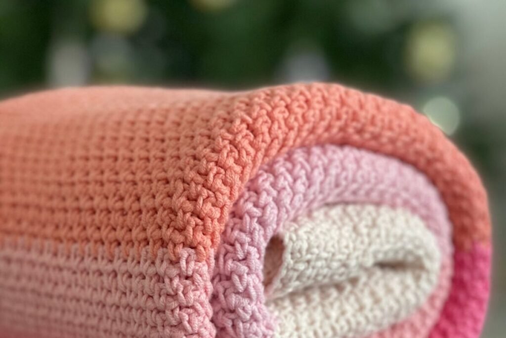 A rolled christmas crochet blanket showing single crochet texture in front of a lit tree