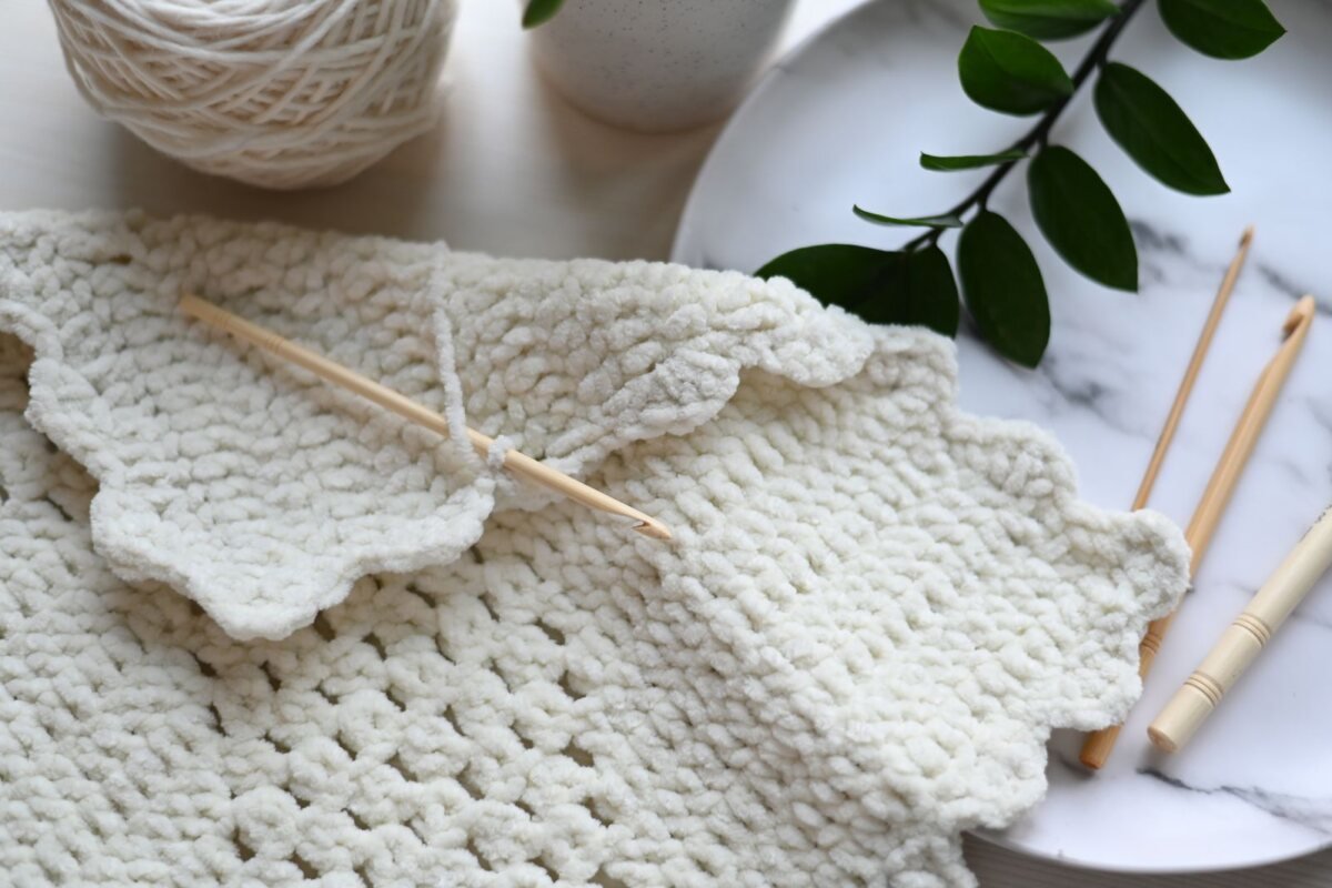 A cream crochet work in progress with wooden crochet hooks and a ball of yarn