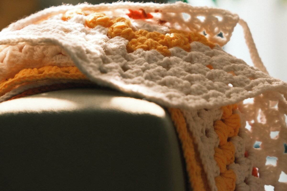 Fall coloured crochet blanket on a sofa arm, the blanket scale a crochet wheat stitch pumpkin panel grows into