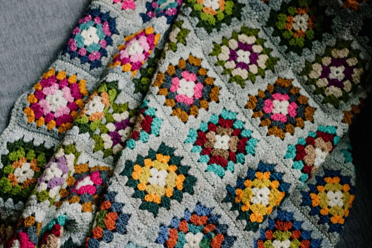 A granny square crochet blanket with grey joining rounds folded on a sofa