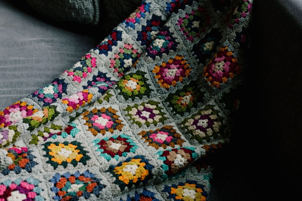 A granny square crochet blanket with grey joining rounds draped over a sofa