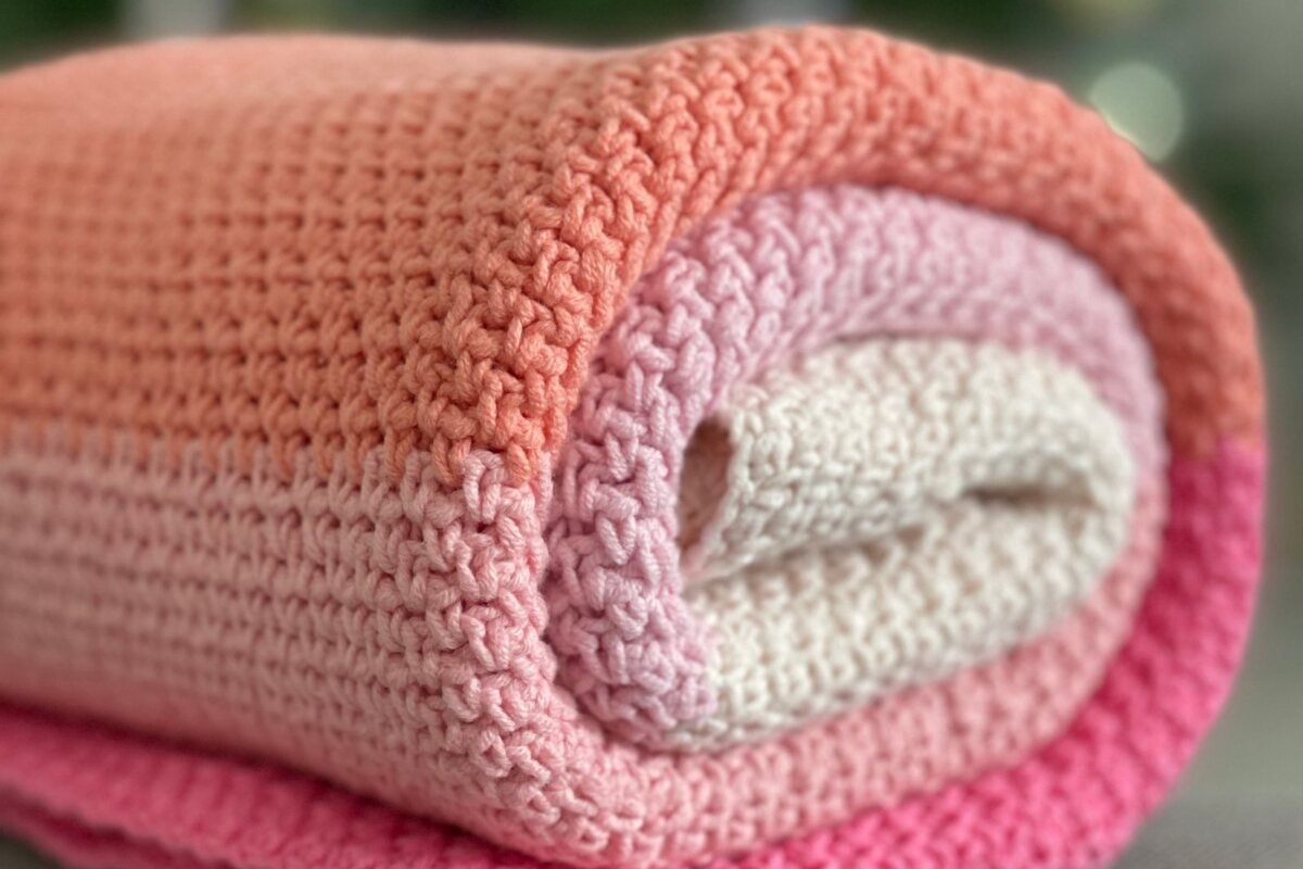 A rolled crochet blanket in coral and pink stripes worked in simple repeating rows