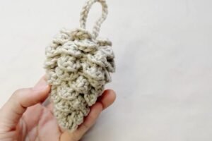 finished crochet pinecone from a free crochet pinecone pattern, held in one hand with a hanging loop