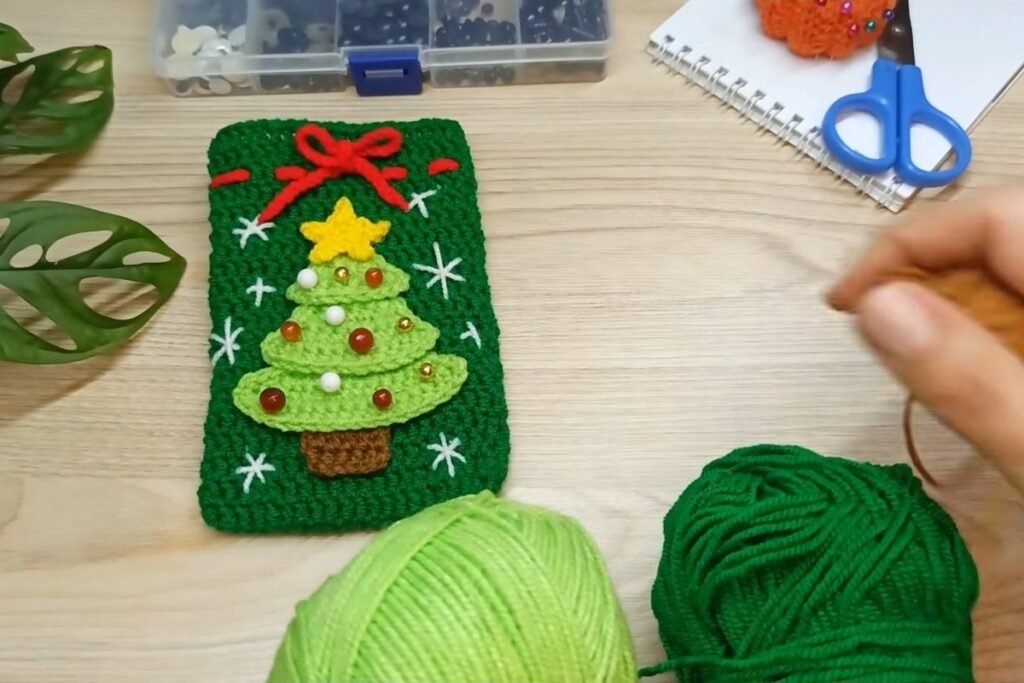 Dark green and light green yarn next to a finished crochet christmas tree gift bag
