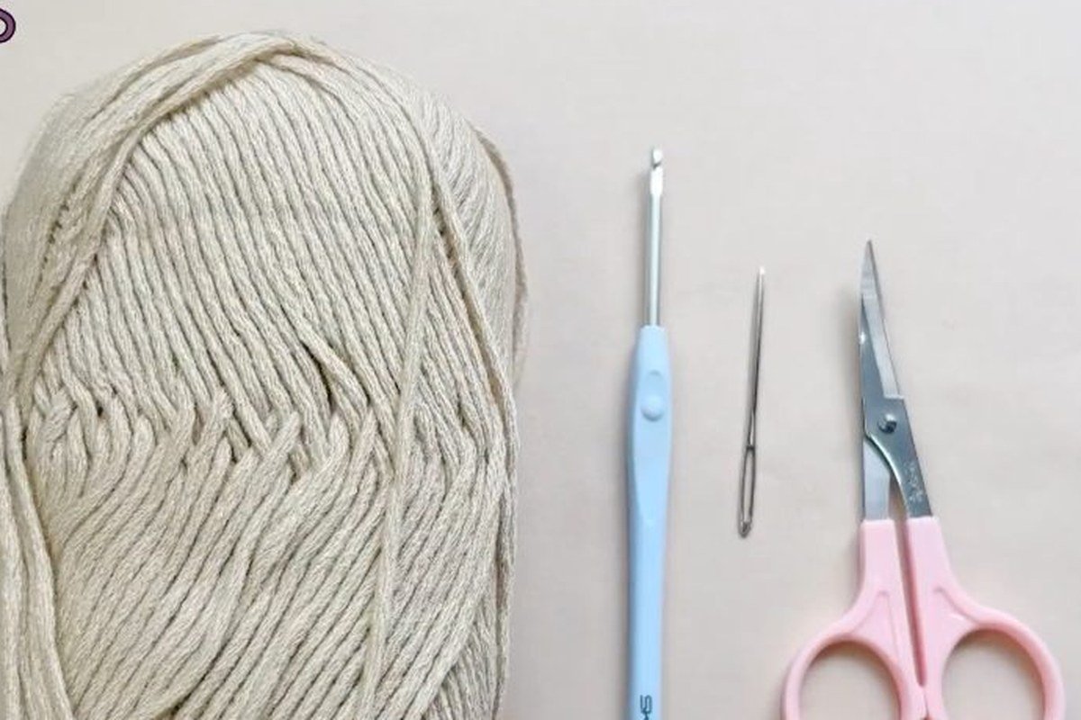 materials for a free crochet pinecone pattern: a ball of beige yarn, a crochet hook, a yarn needle and scissors
