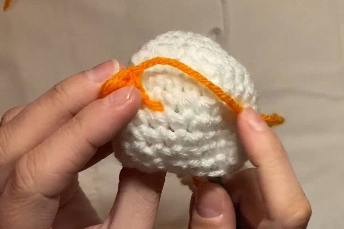 sewing the nose onto the head of a free crochet snowman pattern