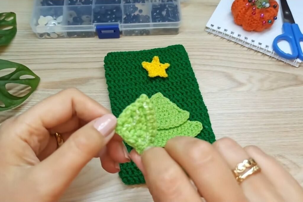 Gluing the three crochet tree tiers onto the front of the green gift bag
