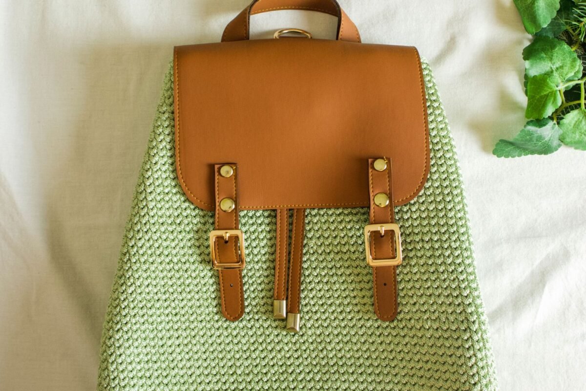 Sage green crochet backpack with a tan leather flap and buckle straps