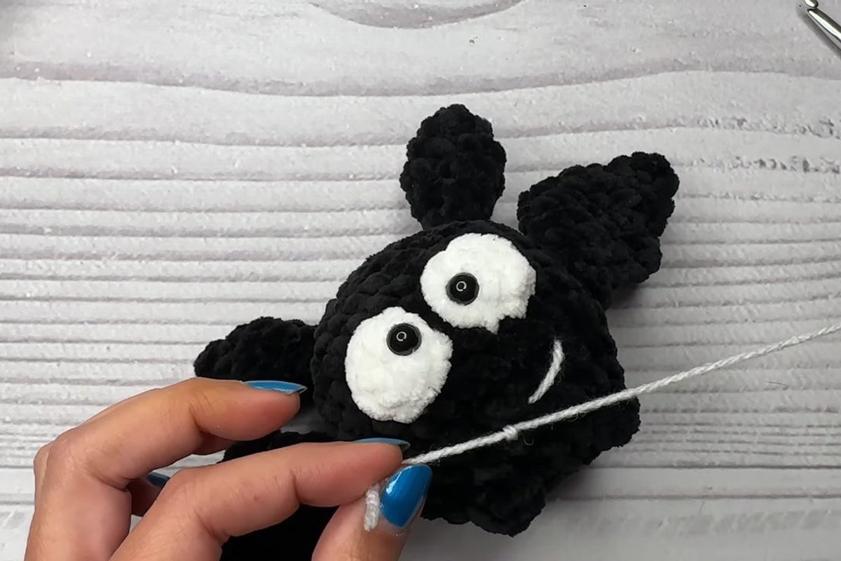 stitching a white smile on a black crochet bat