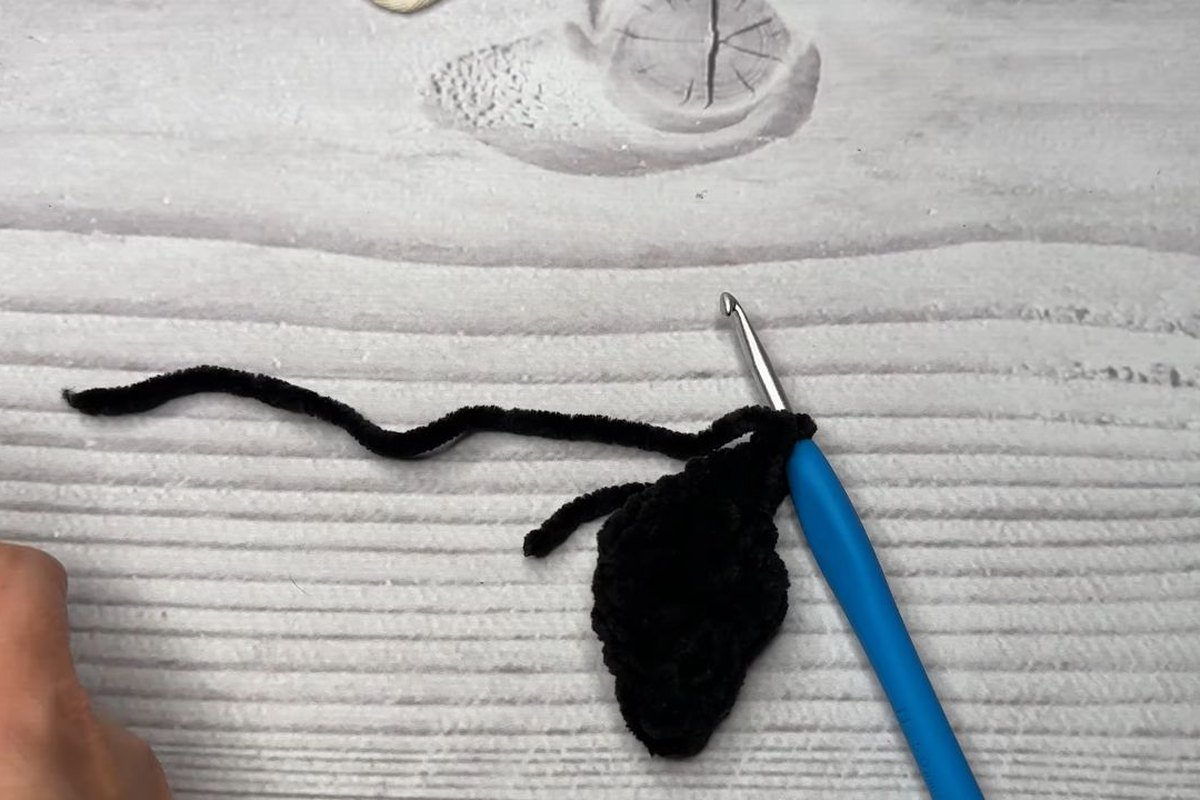 finished small black crochet bat wing on a hook with a long yarn tail