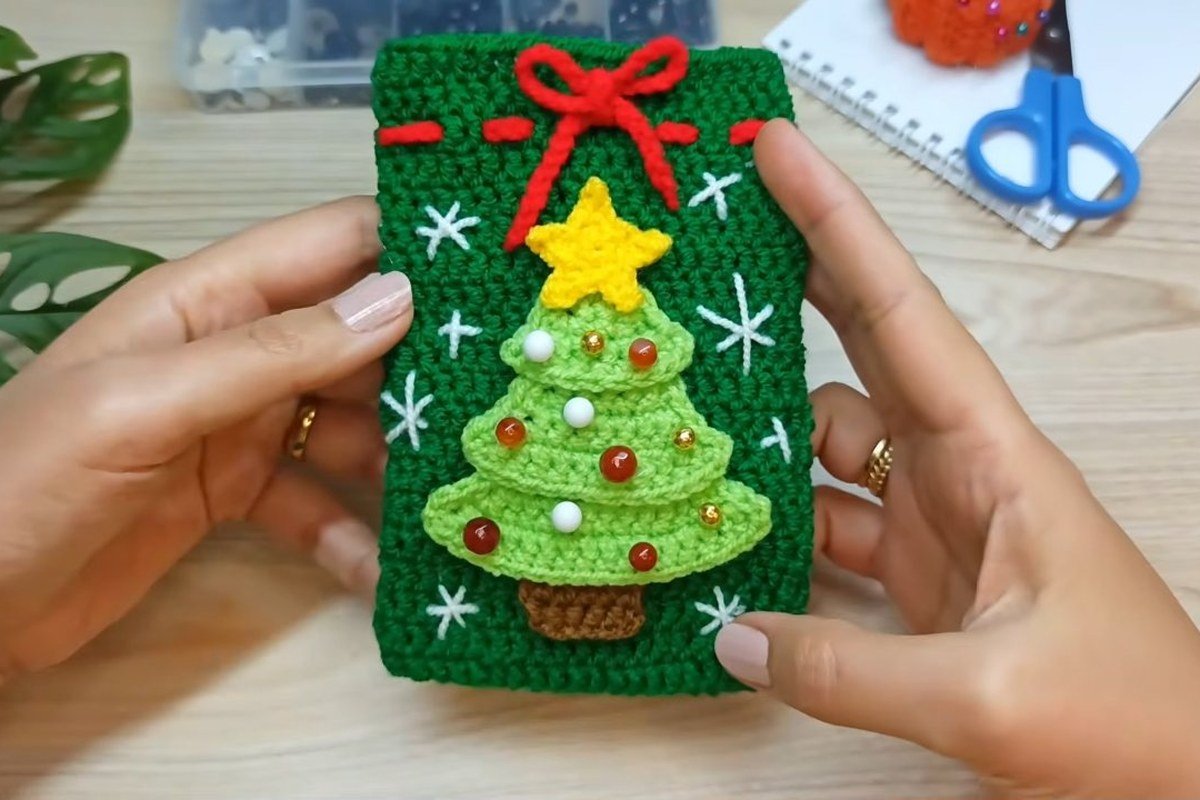 Finished crochet christmas tree gift bag in dark green with a light green three tier tree, yellow star and red drawstring bow