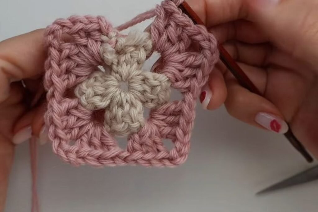 round 2 of the granny square in pink with the yarn tails hidden under the stitches