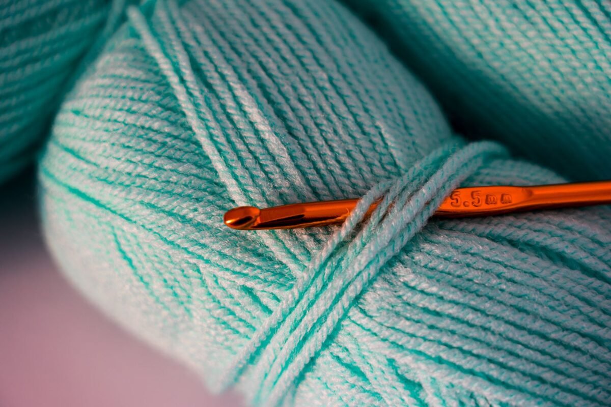 Teal worsted weight yarn with an orange crochet hook resting across the strands