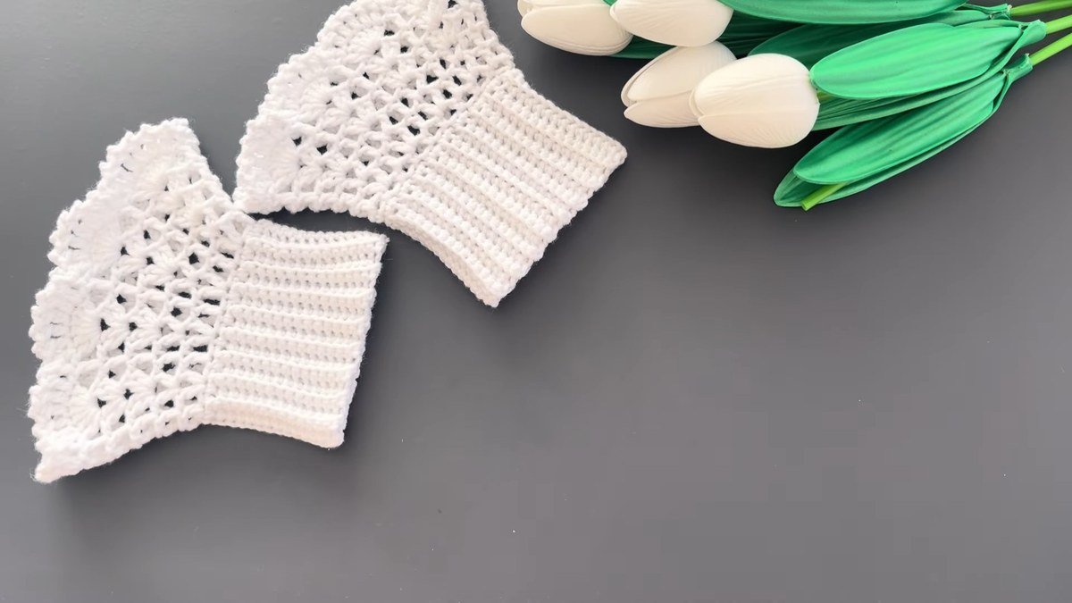 a finished pair of white crochet lace wrist cuffs laid flat next to green tulips