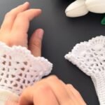 a pair of white crochet lace wrist cuffs worn on the wrist, ribbed band below and lace frill above