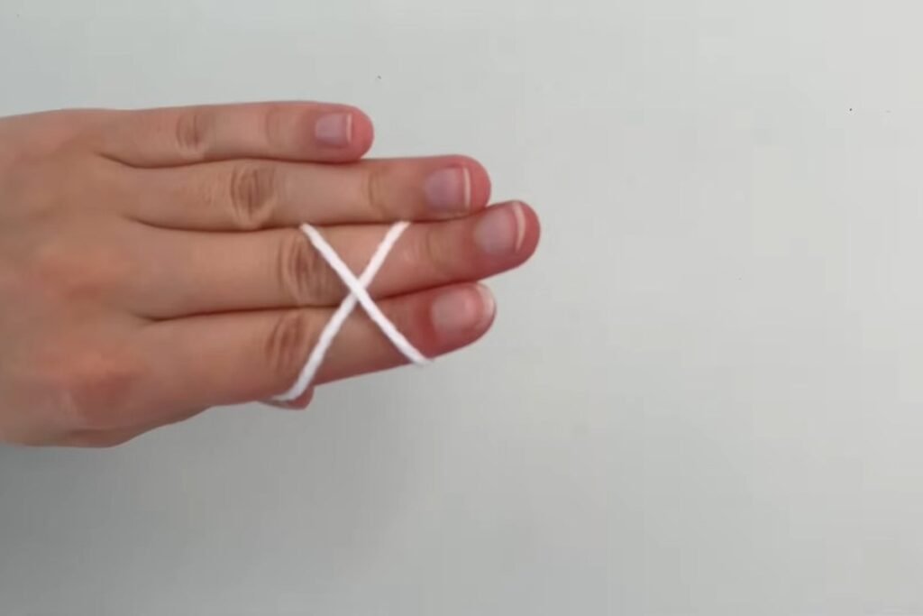White yarn wrapped in a cross around two fingers to start a slip knot