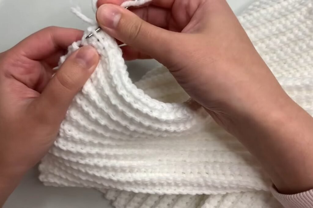Weaving in the yarn tail with a needle along the edge of the easy crochet scarf pattern
