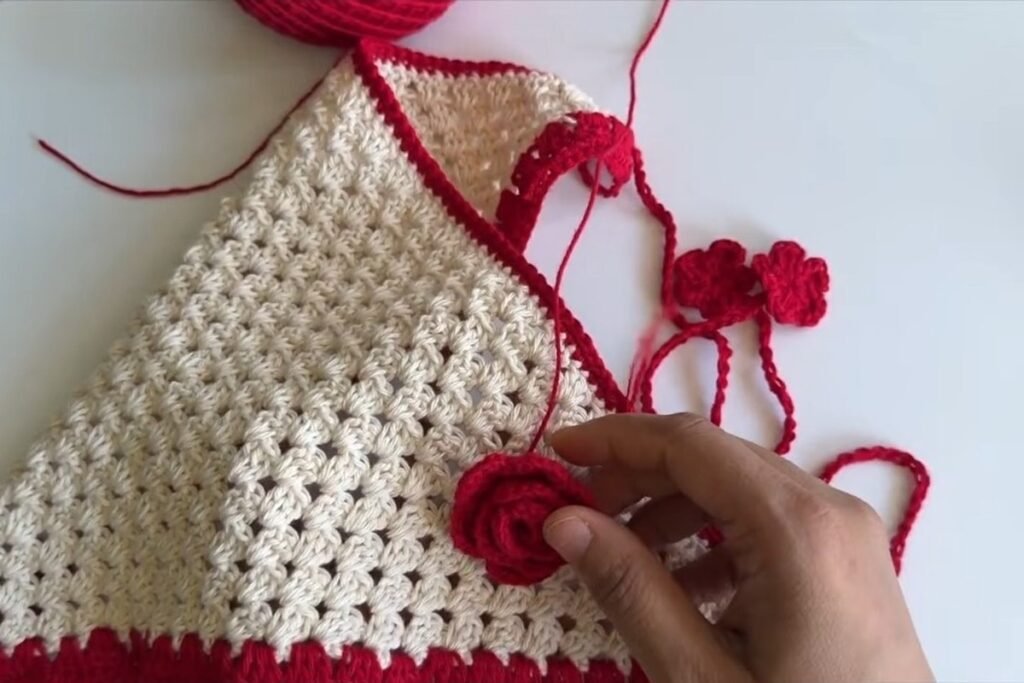 Sewing a red crochet rose onto the corner of the free crochet head scarf pattern