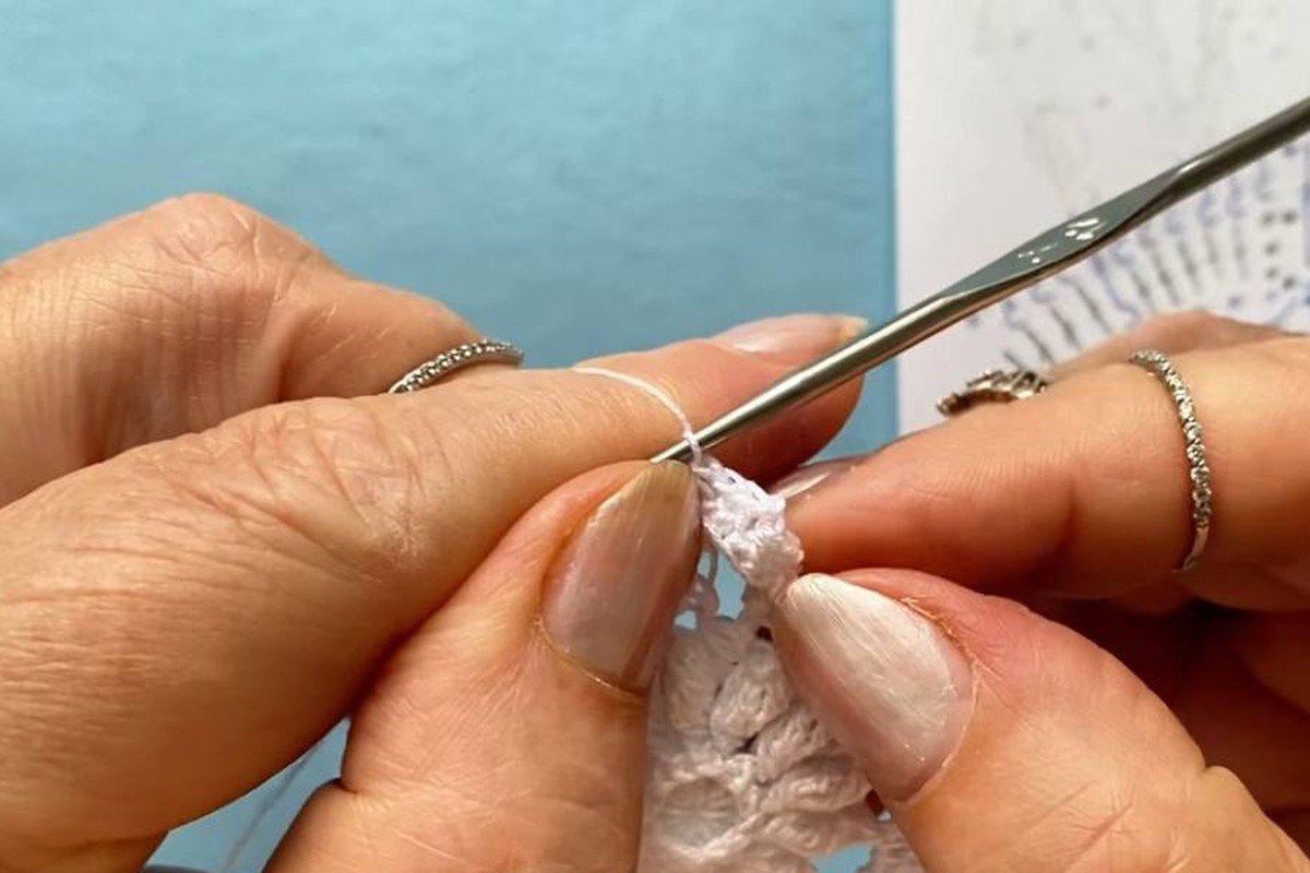 hands working single crochets and treble crochets in round 6 of a crochet snowflake