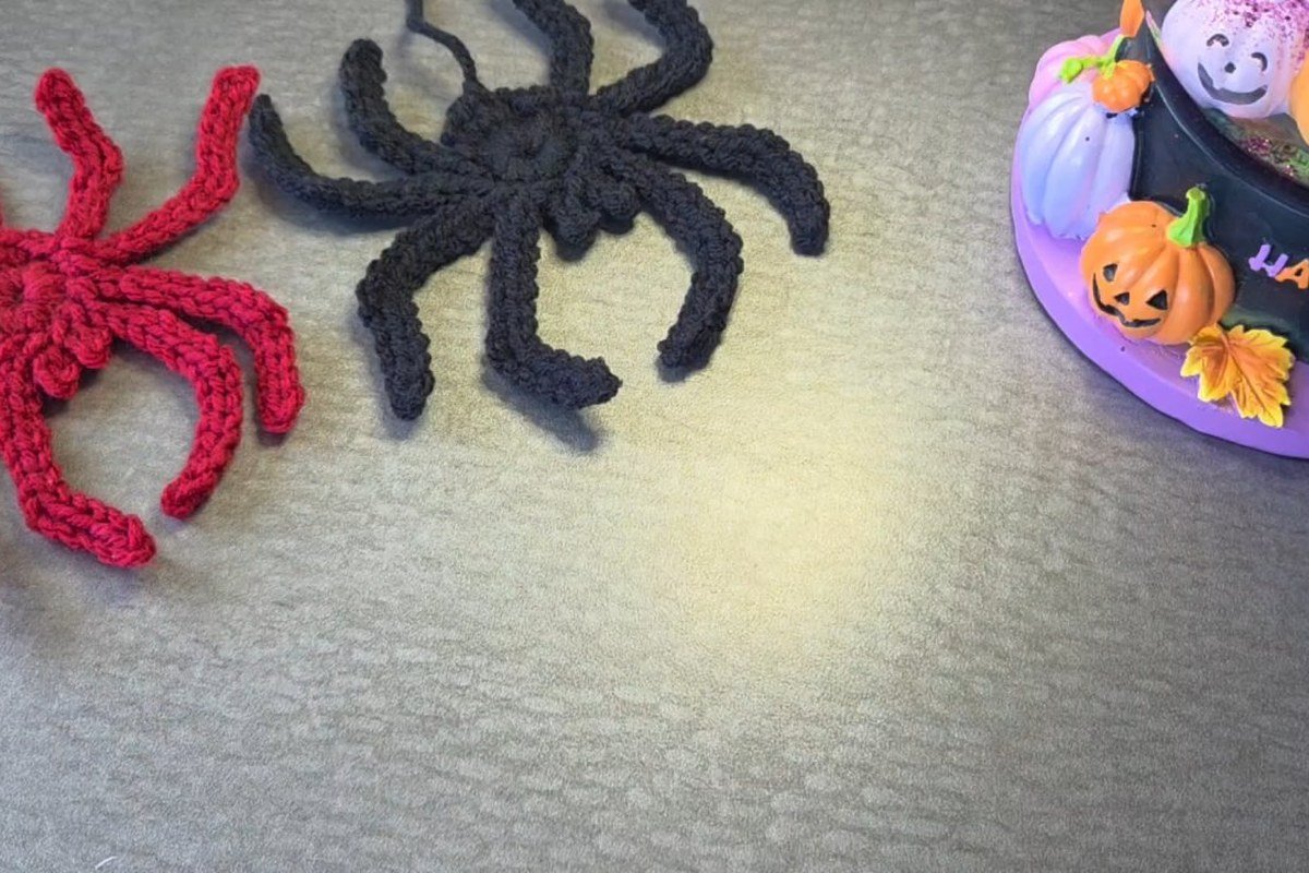 free crochet spider pattern: red, black and grey flat crochet spiders on a table
