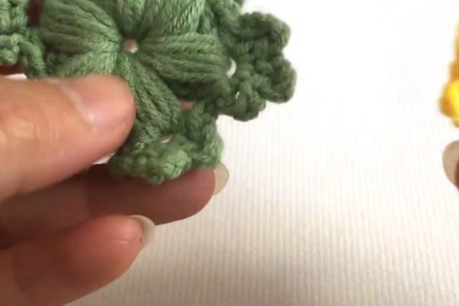 green puff stitch crochet snowflake held in a hand