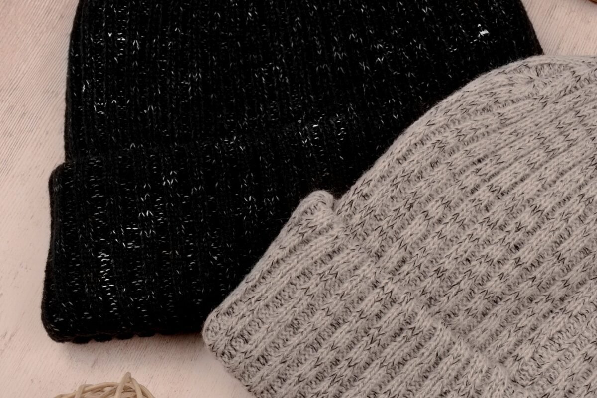 A black and a grey ribbed beanie with folded brims laid flat side by side