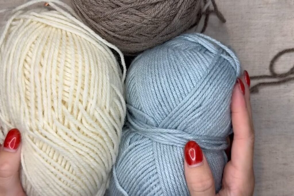 three balls of worsted yarn in cream, blue and taupe for a moss stitch crochet scarf