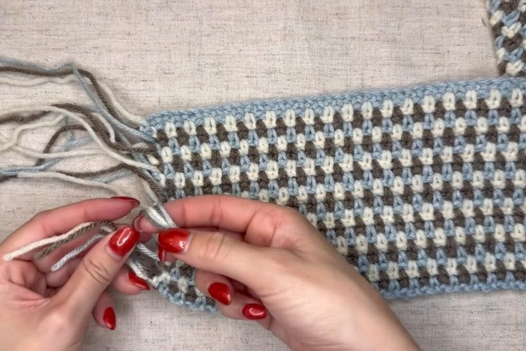 tying yarn tails into knotted tassels on a crochet scarf