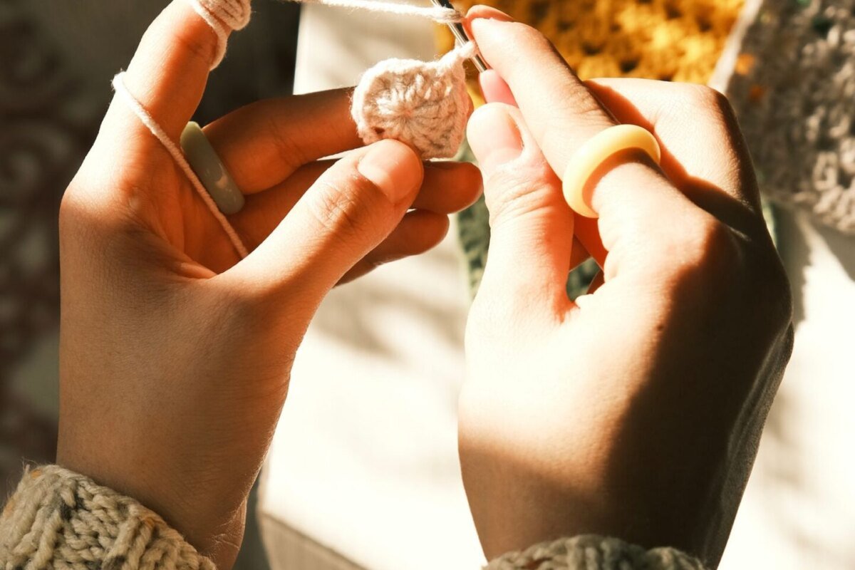 Two hands working the first rounds of a pumpkin granny square in warm daylight