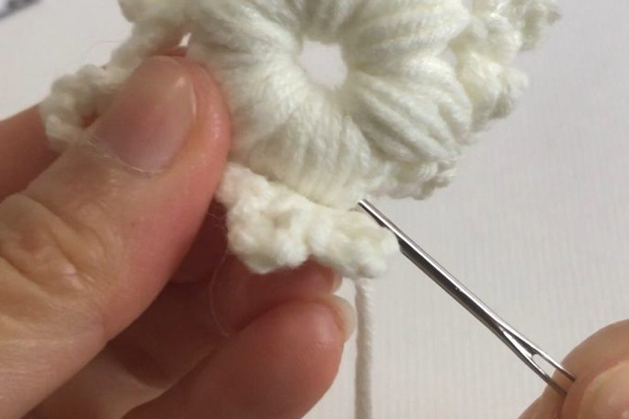weaving in the end of the puff stitch crochet snowflake with a yarn needle