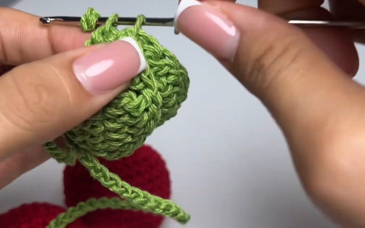 leaf being threaded onto the stem of a crochet cherry keychain