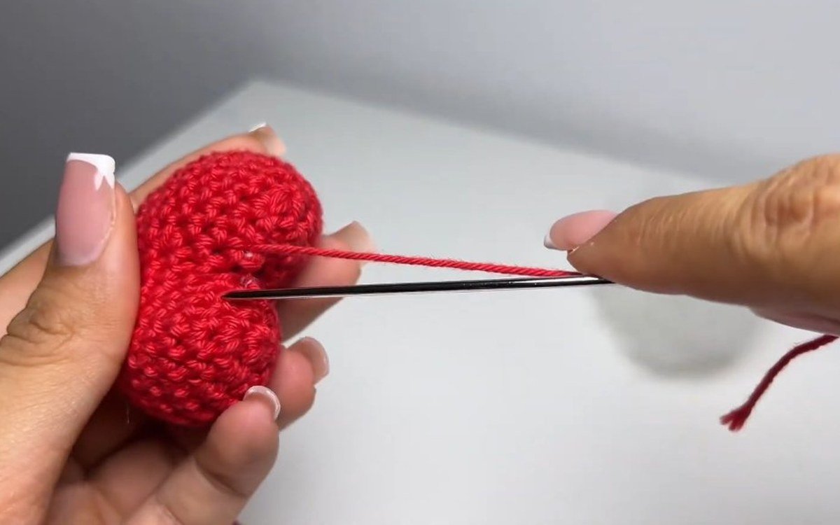 needle sewing the top gap of a heart-shaped crochet cherry keychain cherry