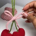 finished crochet cherry keychain with two red heart-shaped cherries, a green stem and a pink bow