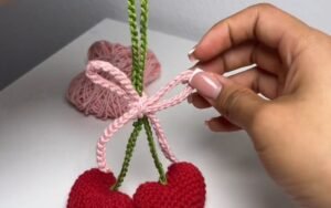 finished crochet cherry keychain with two red heart-shaped cherries, a green stem and a pink bow