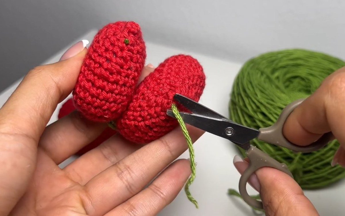 scissors trimming green yarn ends on a crochet cherry keychain