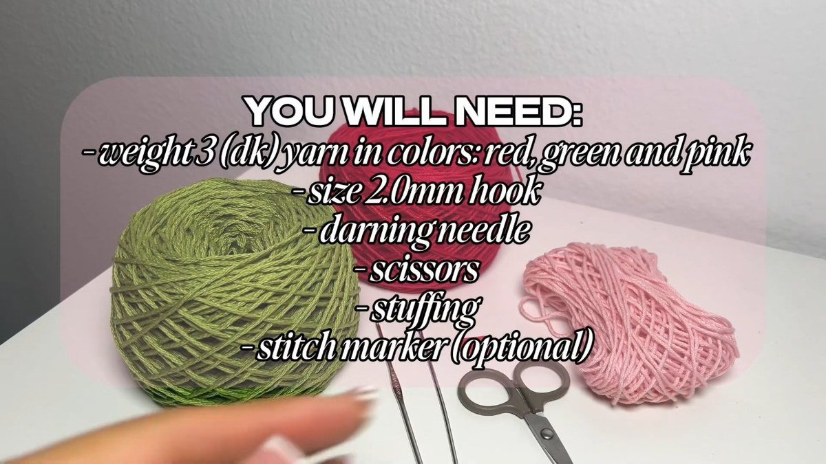 DK yarn in red, green and pink with hooks, a darning needle and scissors for a crochet cherry keychain